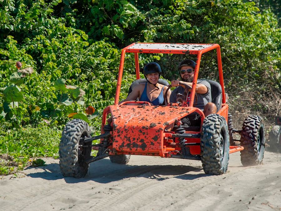 A couple riding a mud-splattered red buggy on a tropical trail