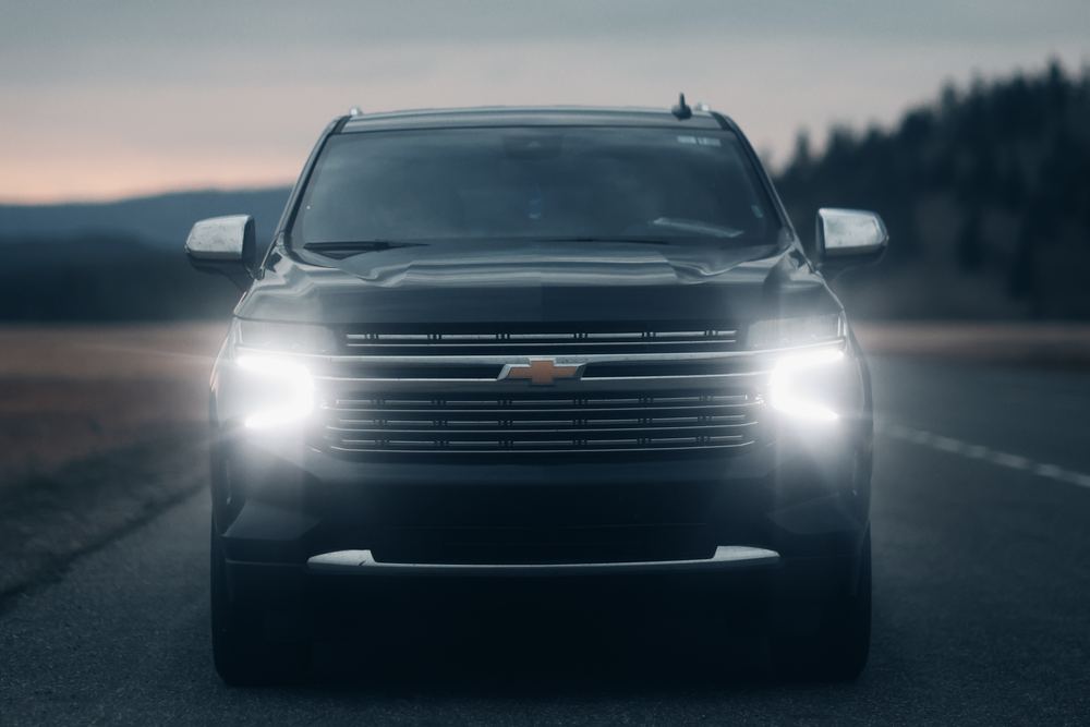 A black Chevrolet Tahoe executive SUV with its headlights on at dusk